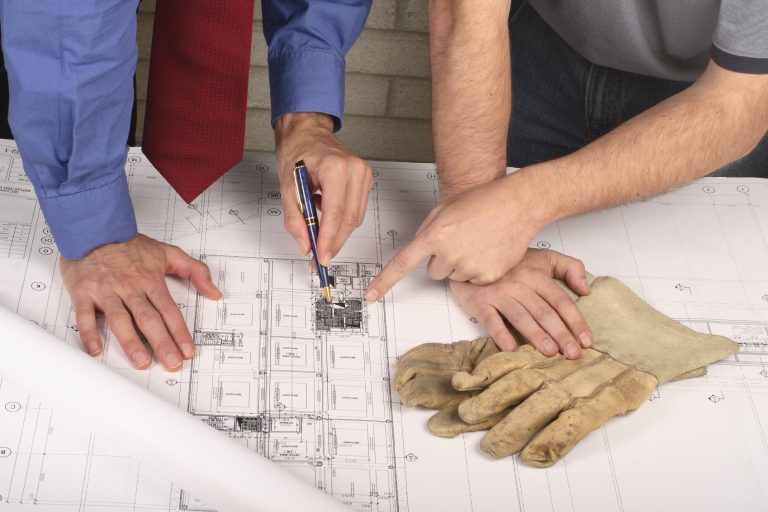 Manos analizando planos arquitectónicos, con guantes de trabajo sobre la mesa.