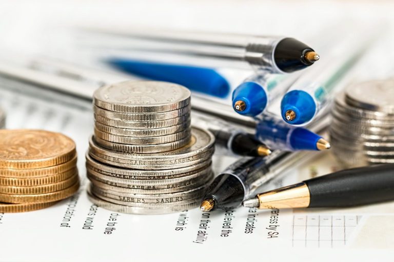 Monedas apiladas junto a bolígrafos y papeles financieros.