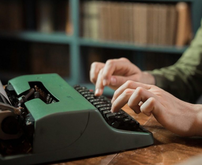 Manos escribiendo en una máquina de escribir sobre una mesa de madera.