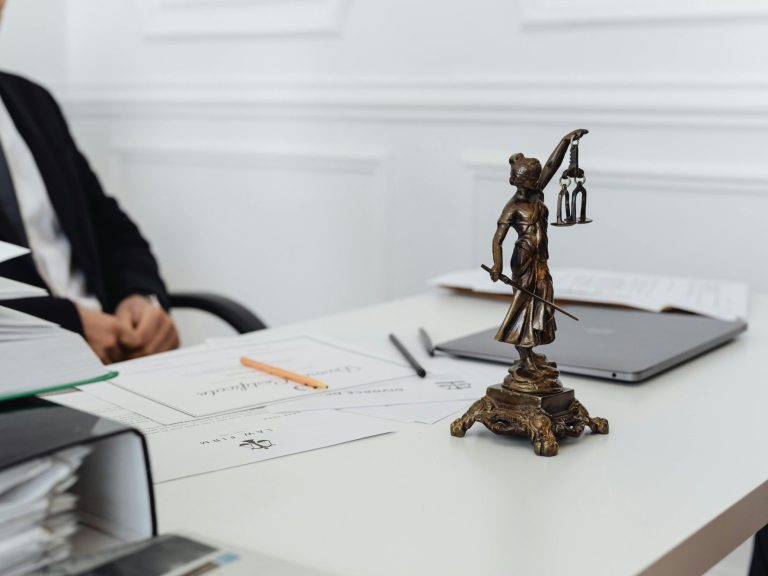 Estatua de una figura sosteniendo una balanza sobre una mesa de oficina.