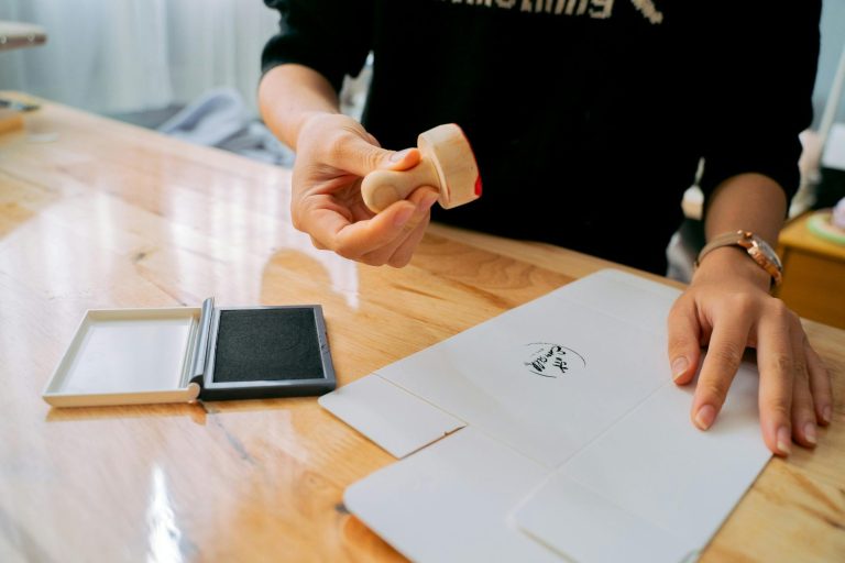 Persona sosteniendo un sello sobre papel en una mesa de madera.